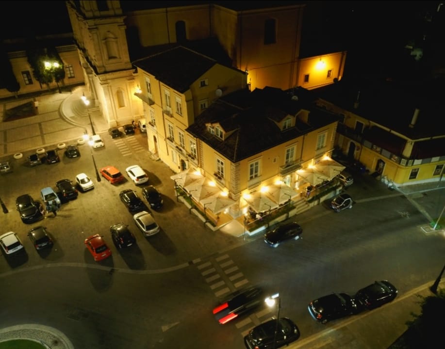 Veduta notturna dall'alto del dehors illuminato di Etoile con ombrelloni bianchi, palazzo giallo e auto in sosta